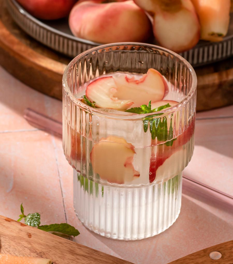 Nahaufnahme eines Glases Wasser, im Hintergrund Obst